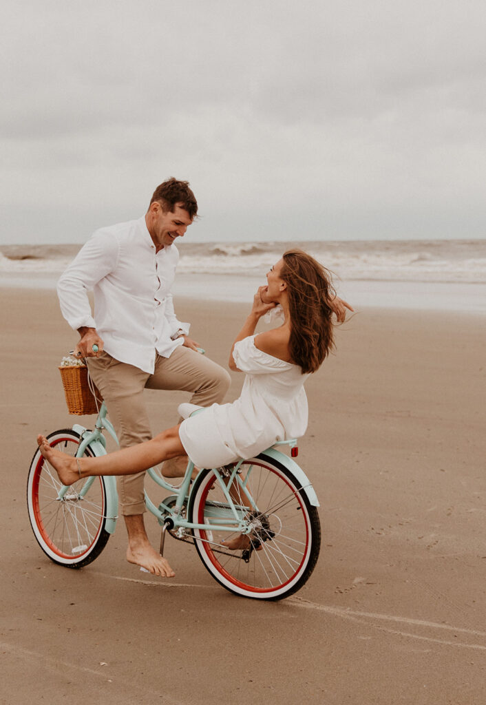 Couple riding a bike on the beach for their engagement 