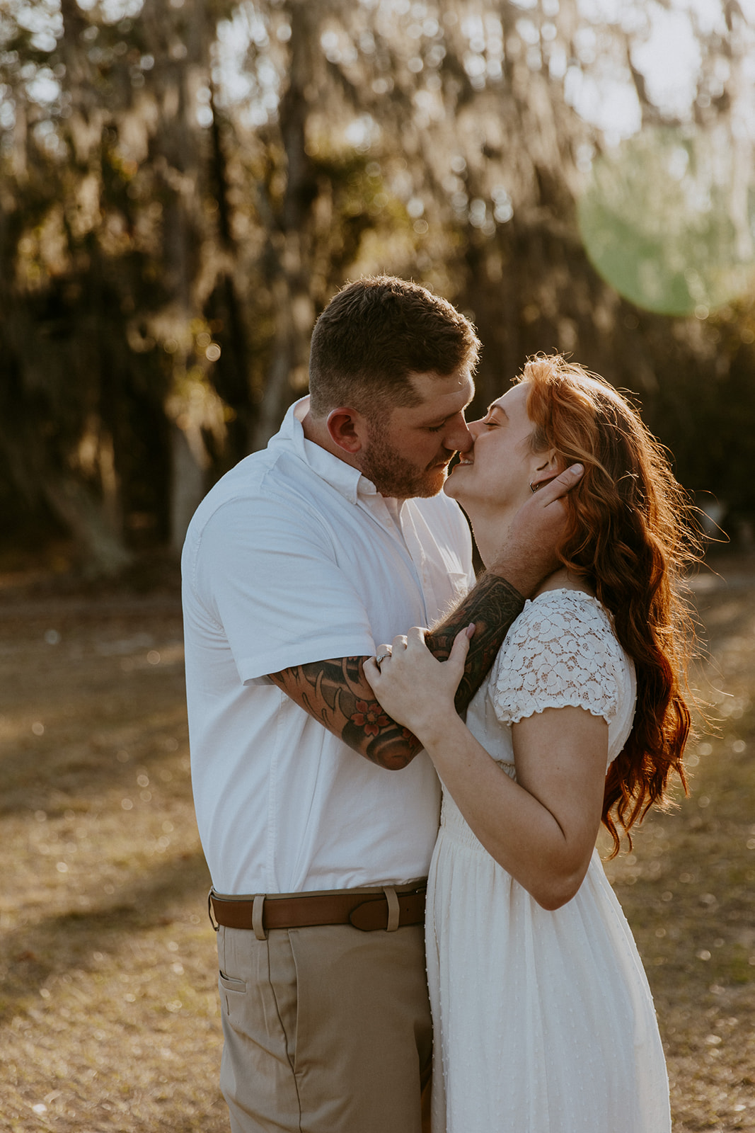 A couple embraces lovingly in a sunlit natural setting, touching foreheads and smiling at each other at their outdoor engagement photos