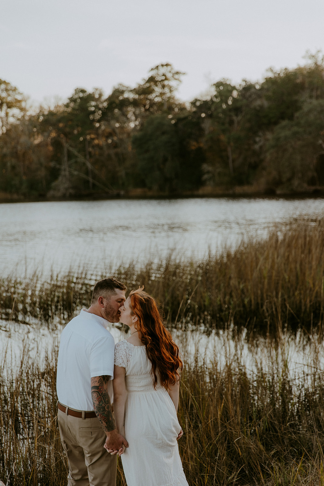 A couple embraces lovingly in a sunlit natural setting, touching foreheads and smiling at each other at their outdoor engagement photos