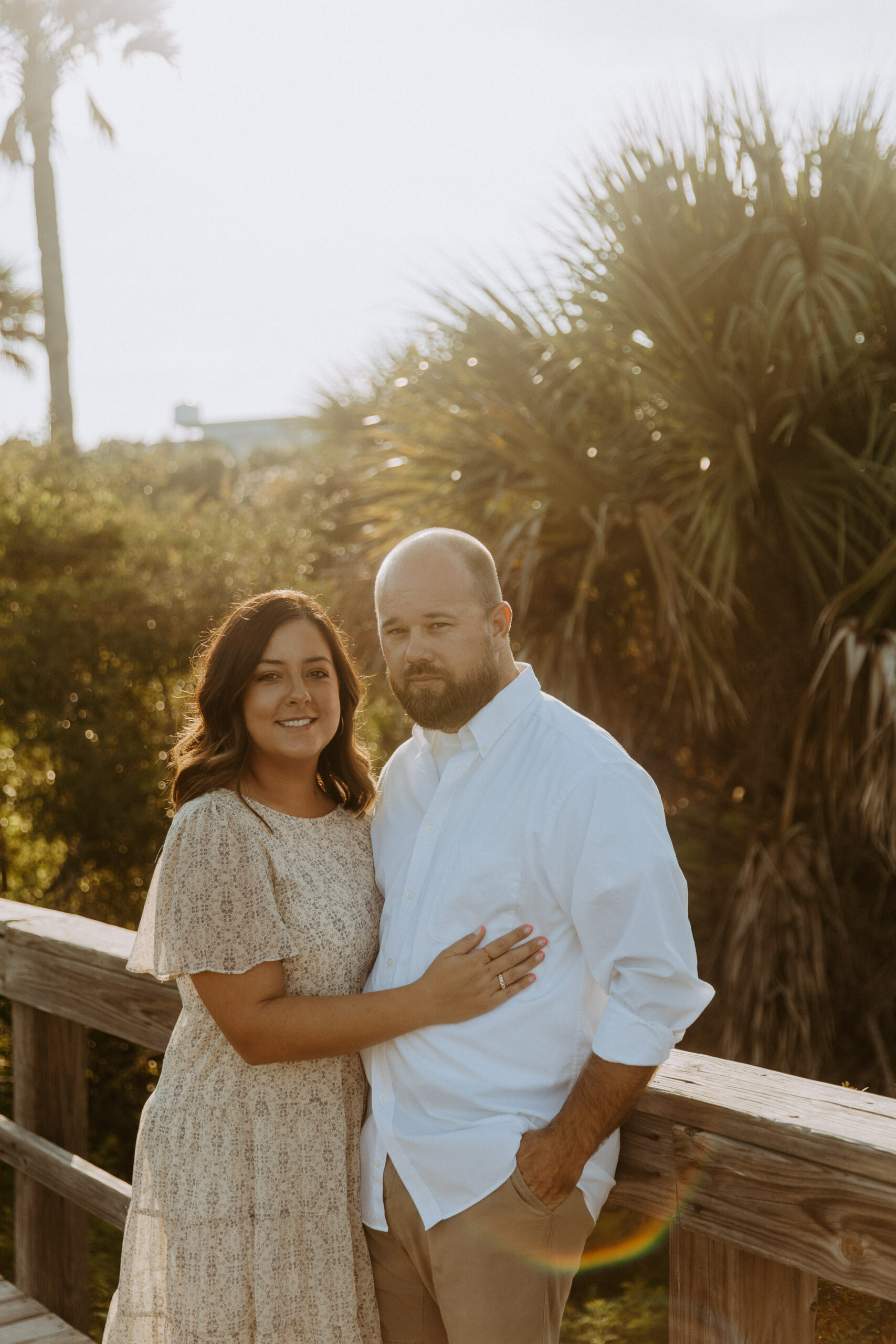 A couple posing together on a wooden walkway amidst tropical foliage at sunset at their anniversary session. 