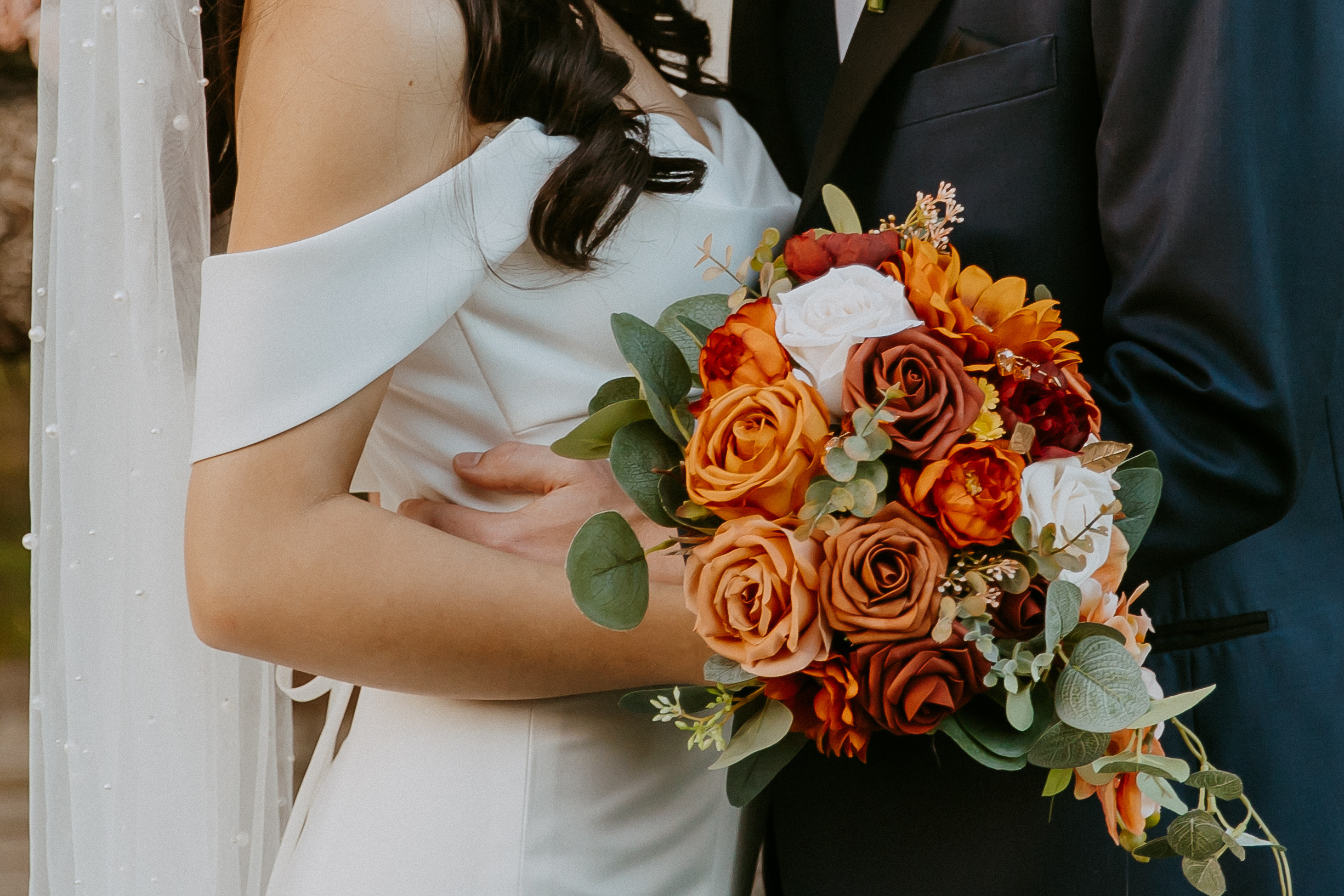 A close-up of a bride and groom holding a vibrant bouquet of flowers.