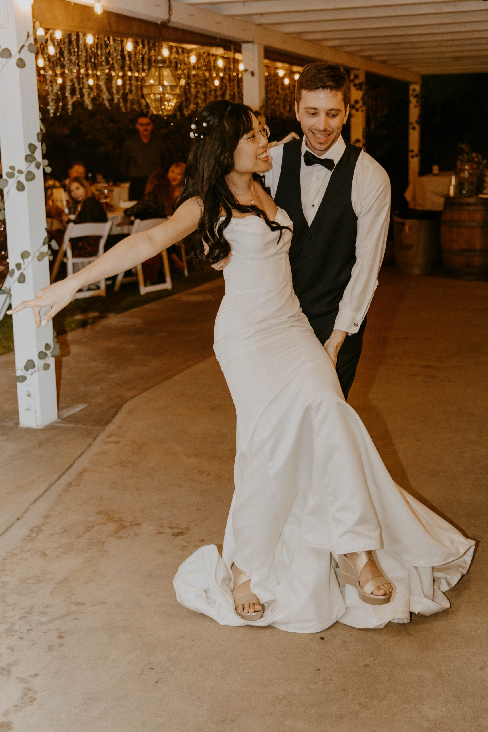A couple shares their first dance at an evening wedding reception under strings of lights at their intimate backyard wedding.