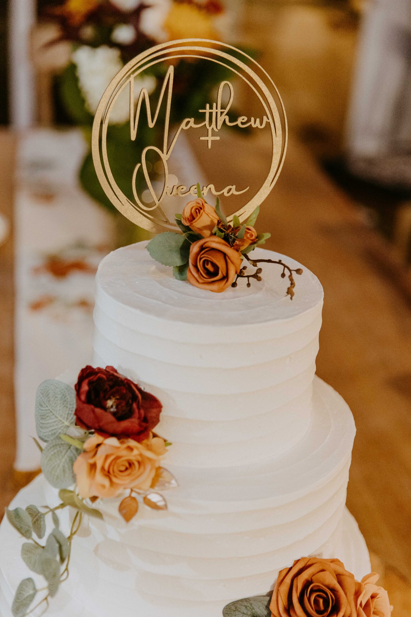Elegant three-tiered wedding cake adorned with roses and a custom name topper.