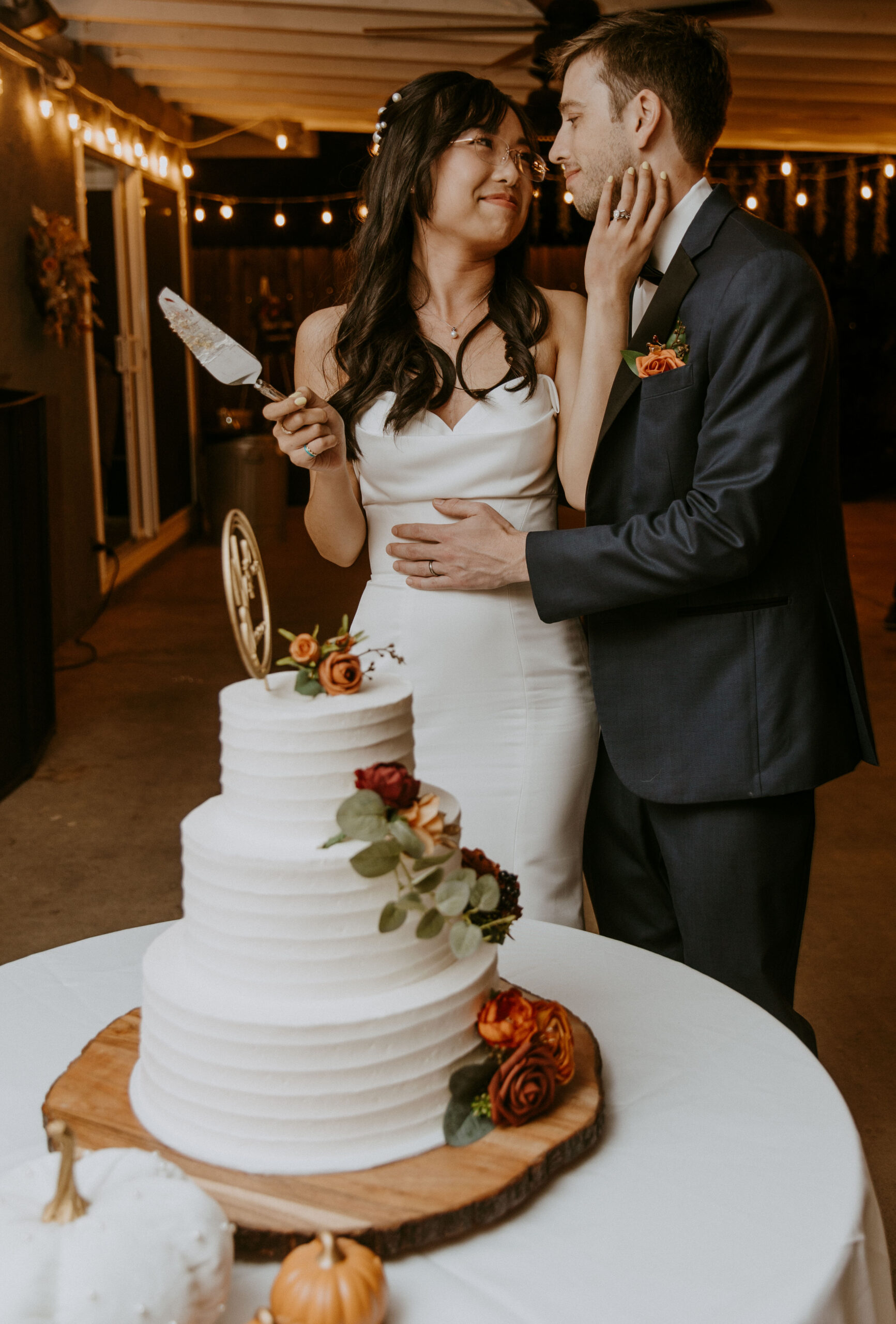 A couple in wedding attire preparing to cut a multi-tiered cake decorated with flowers.