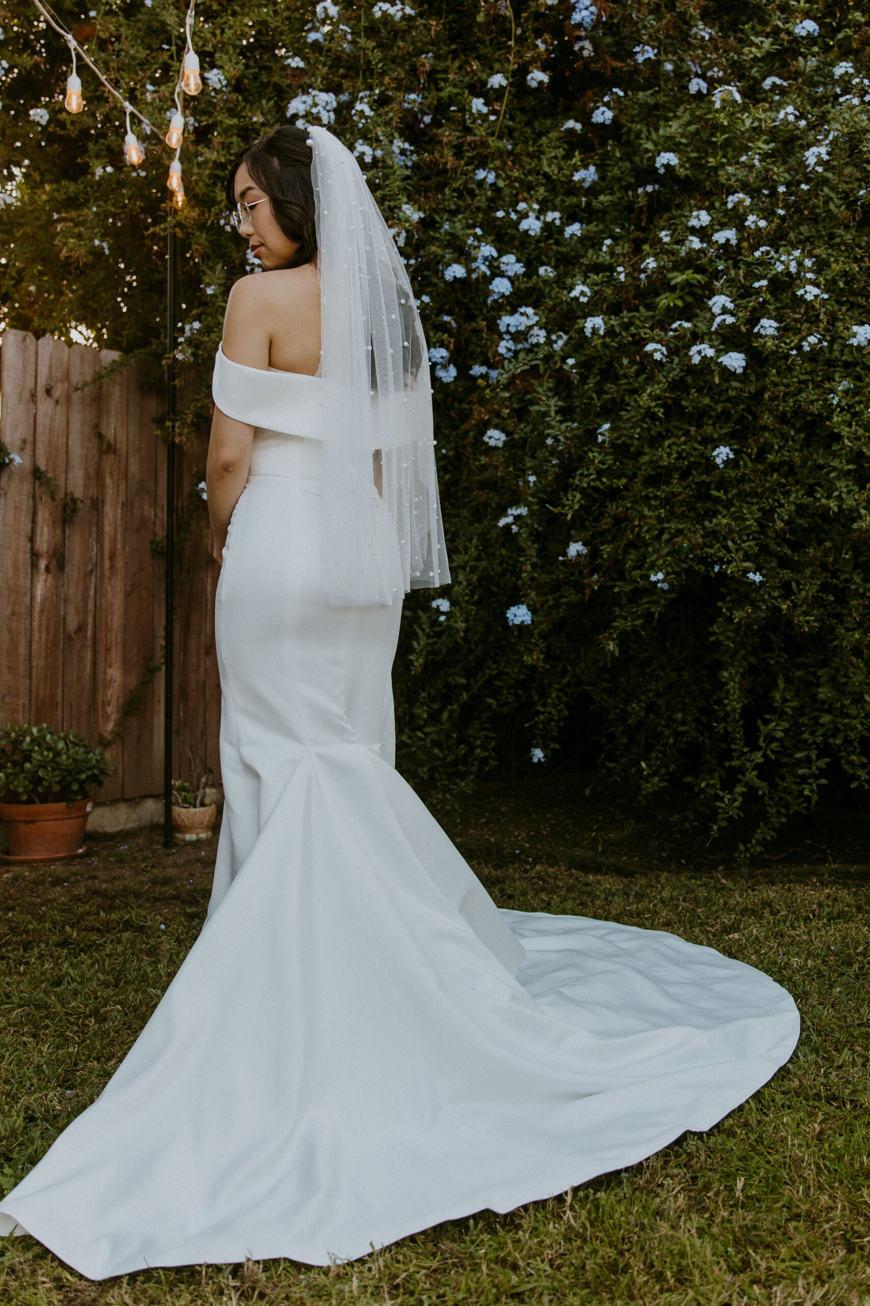Bride in an elegant off-shoulder gown with a veil standing in a garden setting.