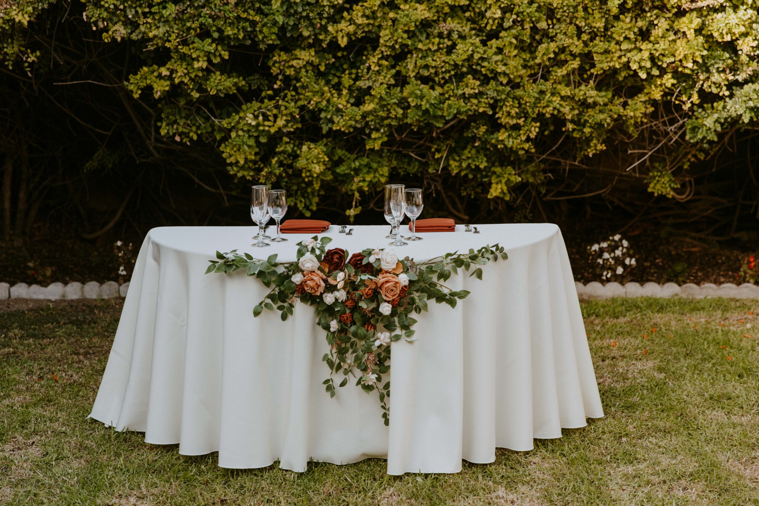 Elegantly set dining table for two with floral centerpiece and candlelight outdoors at an intimate backyard wedding