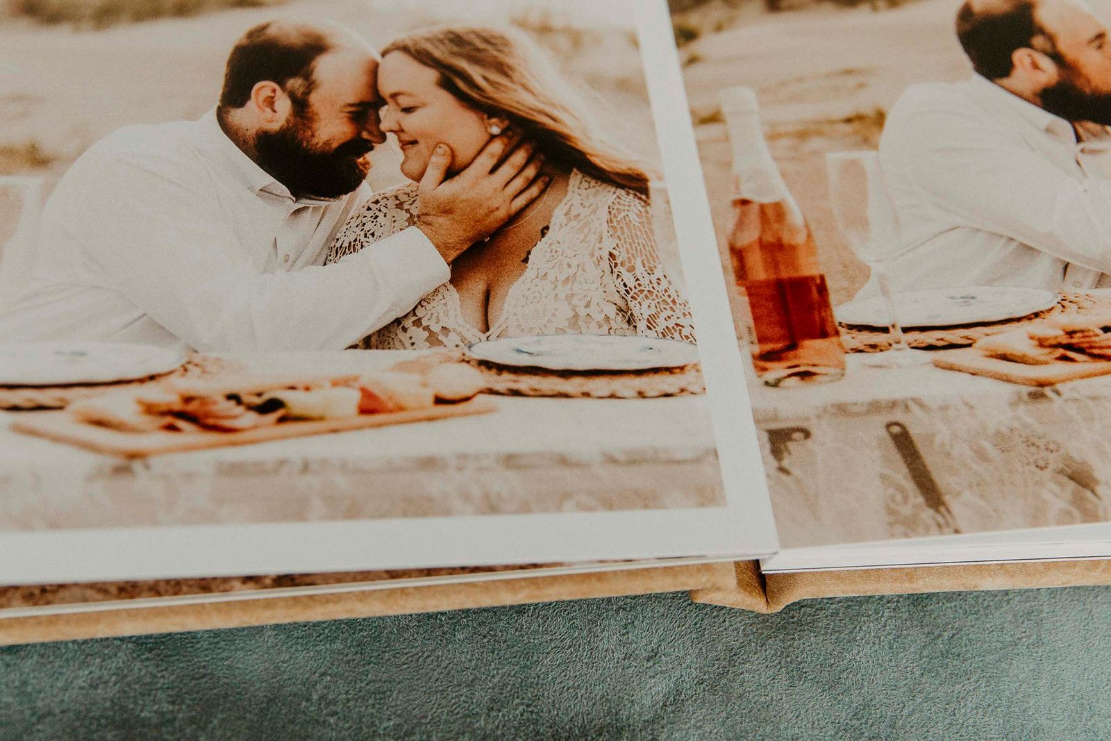 Photo album open to a page showing a couple embracing during a beach picnic, with a bottle of wine nearby.
