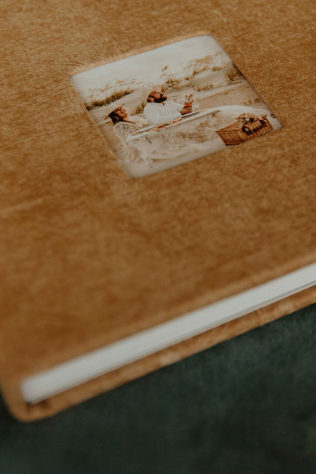 A close-up of a beige photo album with a small picture frame on the cover showing a scenic image, placed on a silver base.