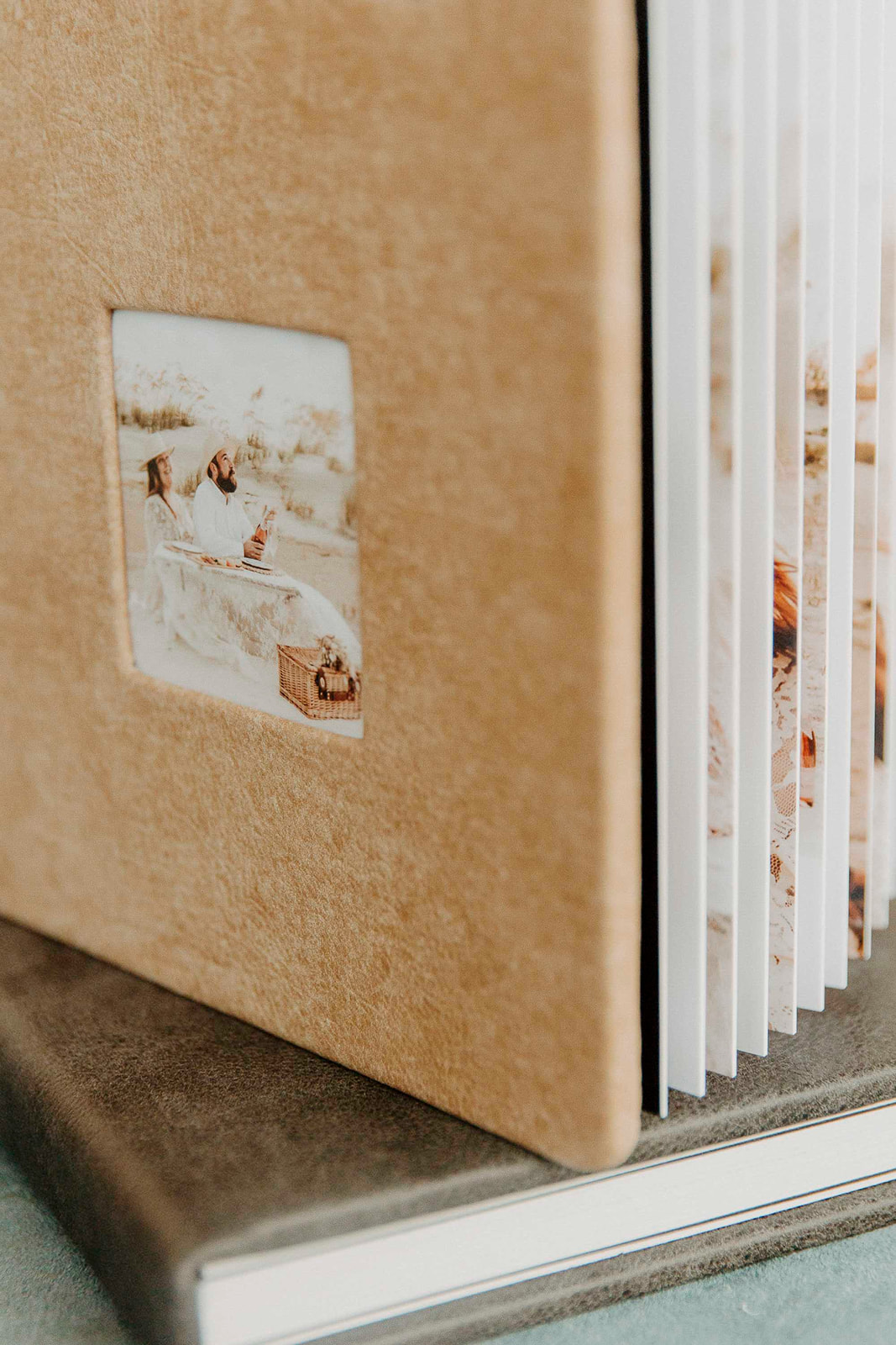 A close-up of a beige wedding photo album with a small picture frame on the cover showing a scenic image, placed on a silver base.
