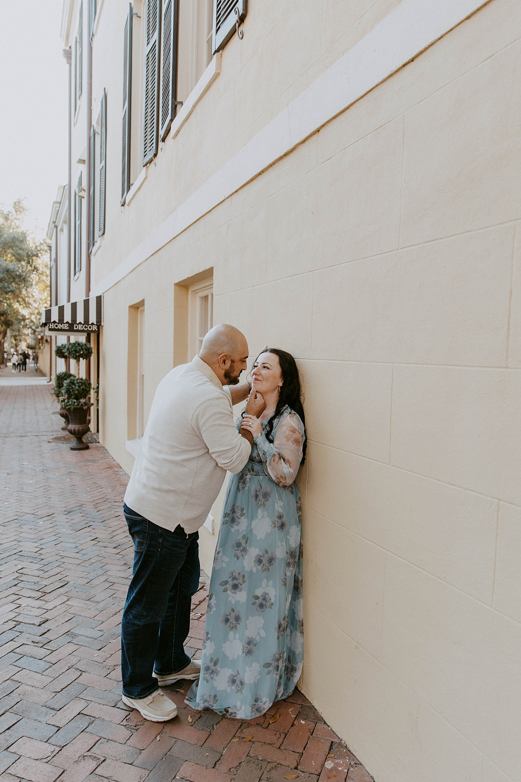 A man and a woman with long dark hair outdoors in a garden-like setting. Both have their eyes closed, showing a moment of affection in Downtown Historic district savannah ga