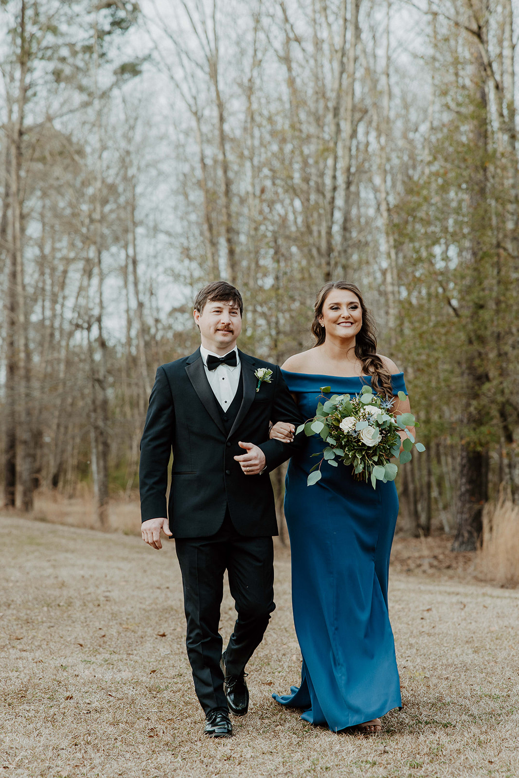 A bride and groom stand facing an officiant during their outdoor wedding ceremony, with a building visible in the background. Flowers are in the foreground at  The Venues at Ogeechee Tech
