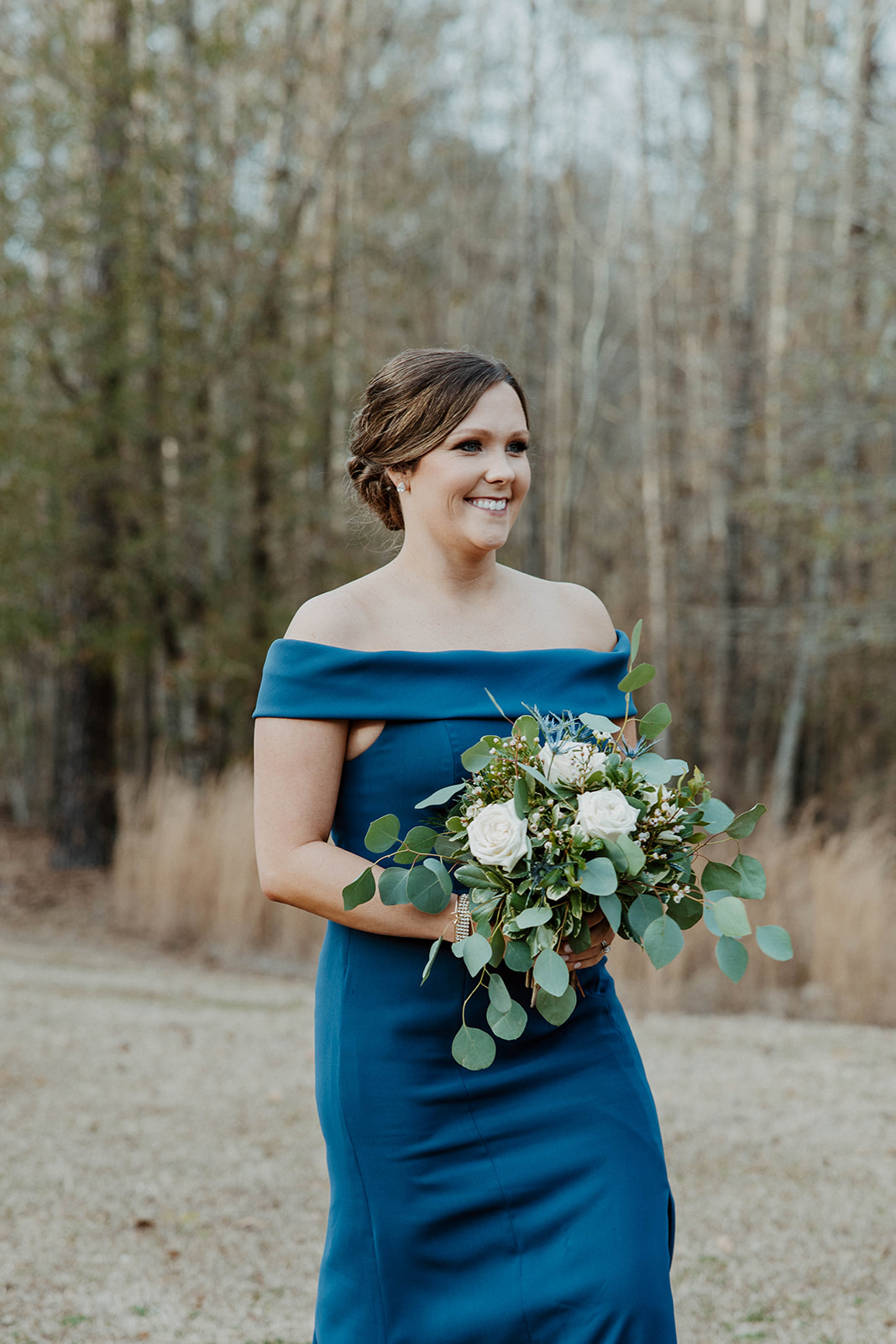 A bride and groom stand facing an officiant during their outdoor wedding ceremony, with a building visible in the background. Flowers are in the foreground at  The Venues at Ogeechee Tech