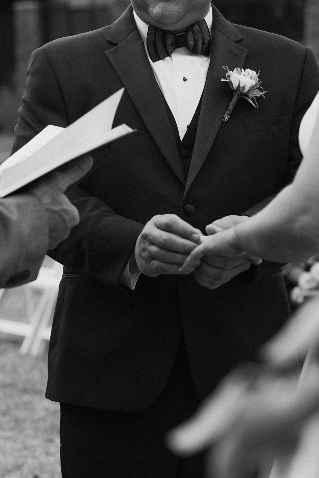 A person in a black suit and bow tie places a ring on the finger of a person in a white wedding dress during a ceremony at The Venues at Ogeechee Tech
