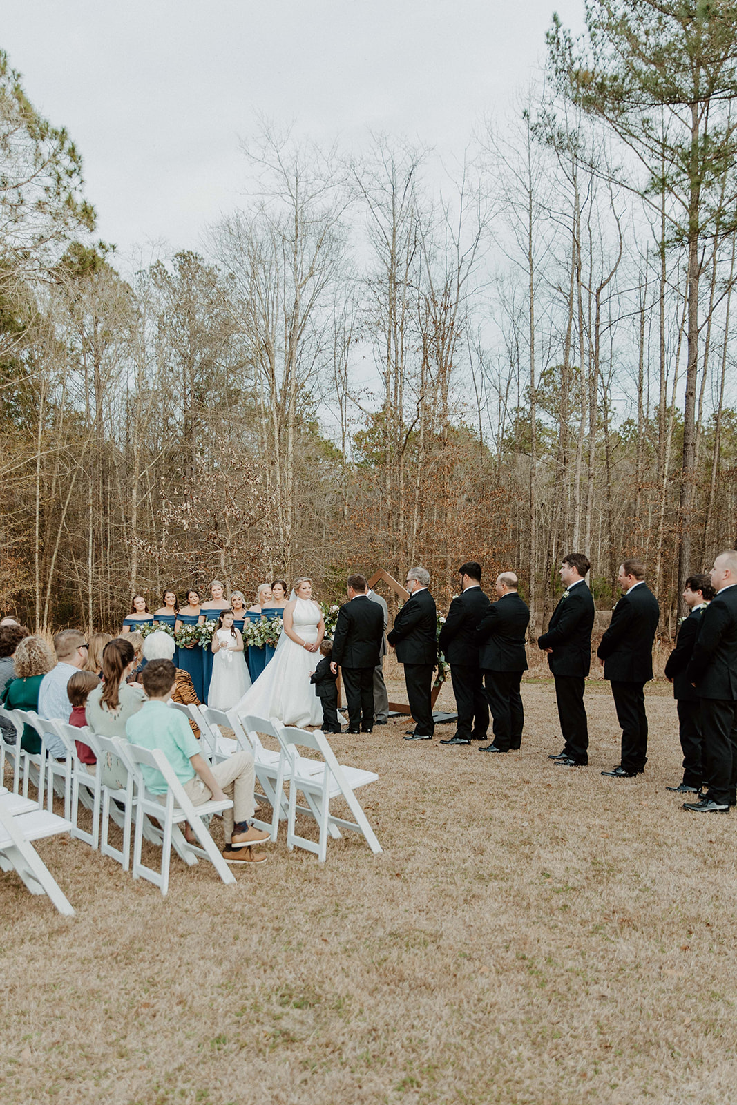 A crowd of people sits on white folding chairs set up on a lawn in front of a modern building with large windows at The Venues at Ogeechee Tech

