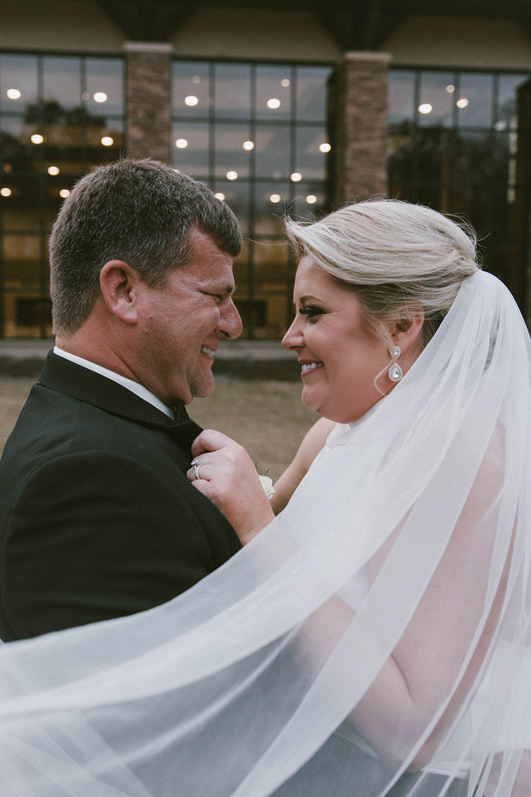 A person in a black suit and bow tie places a ring on the finger of a person in a white wedding dress during a ceremony at The Venues at Ogeechee Tech
