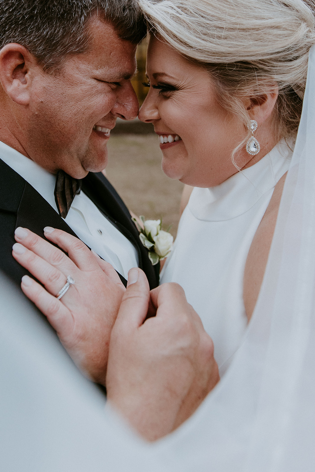 A bride and groom embrace outside a building with large windows. The bride's veil is flowing, and they both have their eyes closed. Trees and foliage are in the background at The Venues at Ogeechee Tech
