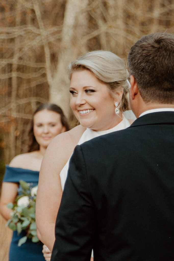 A person in a black suit and bow tie places a ring on the finger of a person in a white wedding dress during a ceremony at The Venues at Ogeechee Tech
