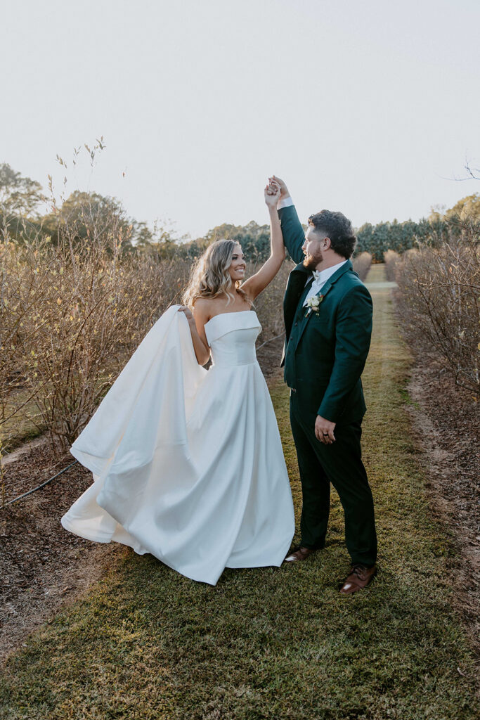 A bride in a white gown and a groom in a dark suit hold hands and dance outdoors on a grassy path, surrounded by autumnal trees. -must have wedding poses