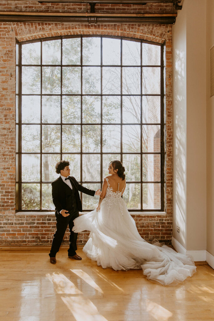 A bride in a white gown and a groom in a dark suit hold hands and dance outdoors on a grassy path, surrounded by autumnal trees. -must have wedding poses