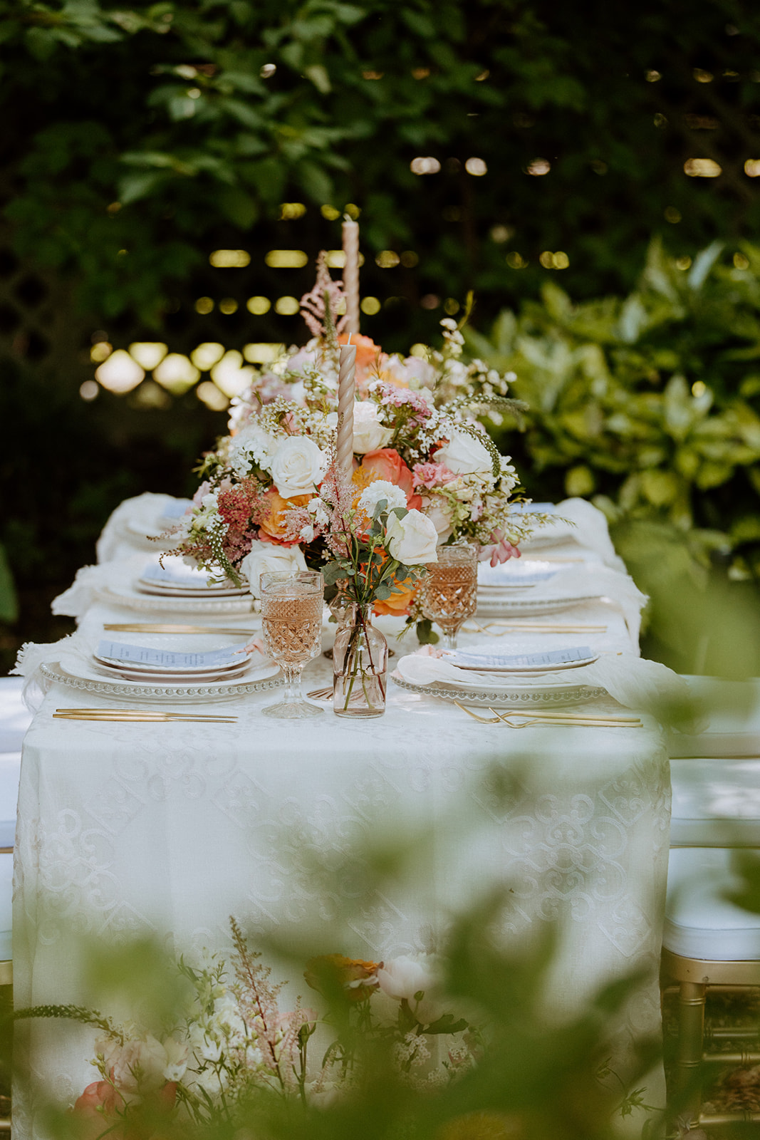 A table set outdoors with floral centerpieces, white plates, glassware, and neatly arranged cutlery, surrounded by lush greenery at Wildflower 301