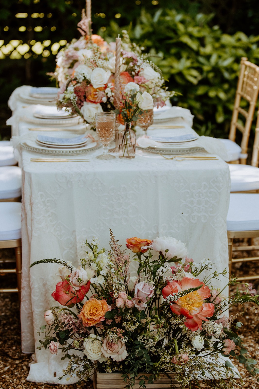 A table set outdoors with floral centerpieces, white plates, glassware, and neatly arranged cutlery, surrounded by lush greenery at Wildflower 301