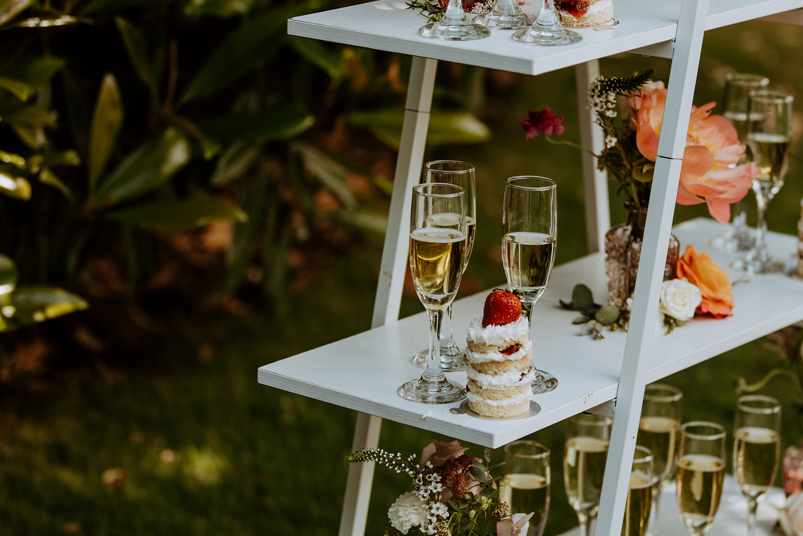 A table set outdoors with floral centerpieces, white plates, glassware, and neatly arranged cutlery, surrounded by lush greenery at Wildflower 301