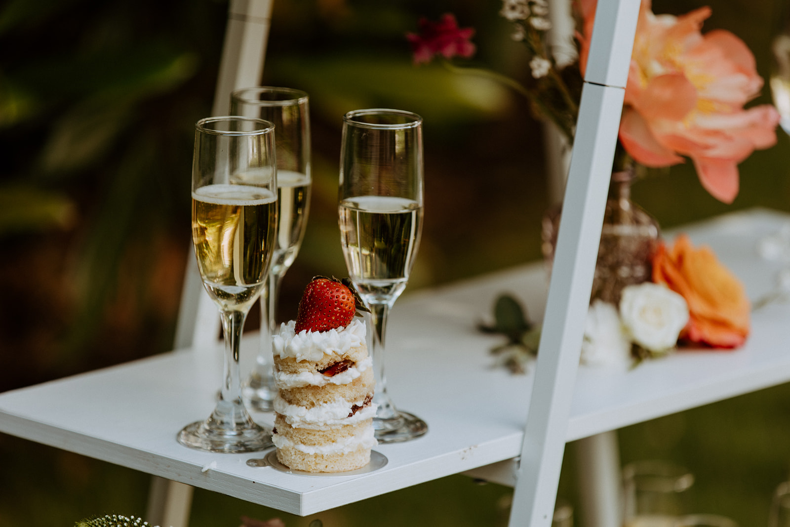 A table set outdoors with floral centerpieces, white plates, glassware, and neatly arranged cutlery, surrounded by lush greenery at Wildflower 301