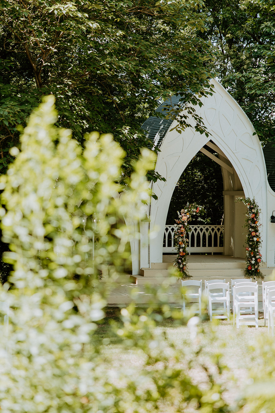 A bride and groom walk down an outdoor aisle holding hands, with empty chairs and an arch structure in the background at wildflower 301