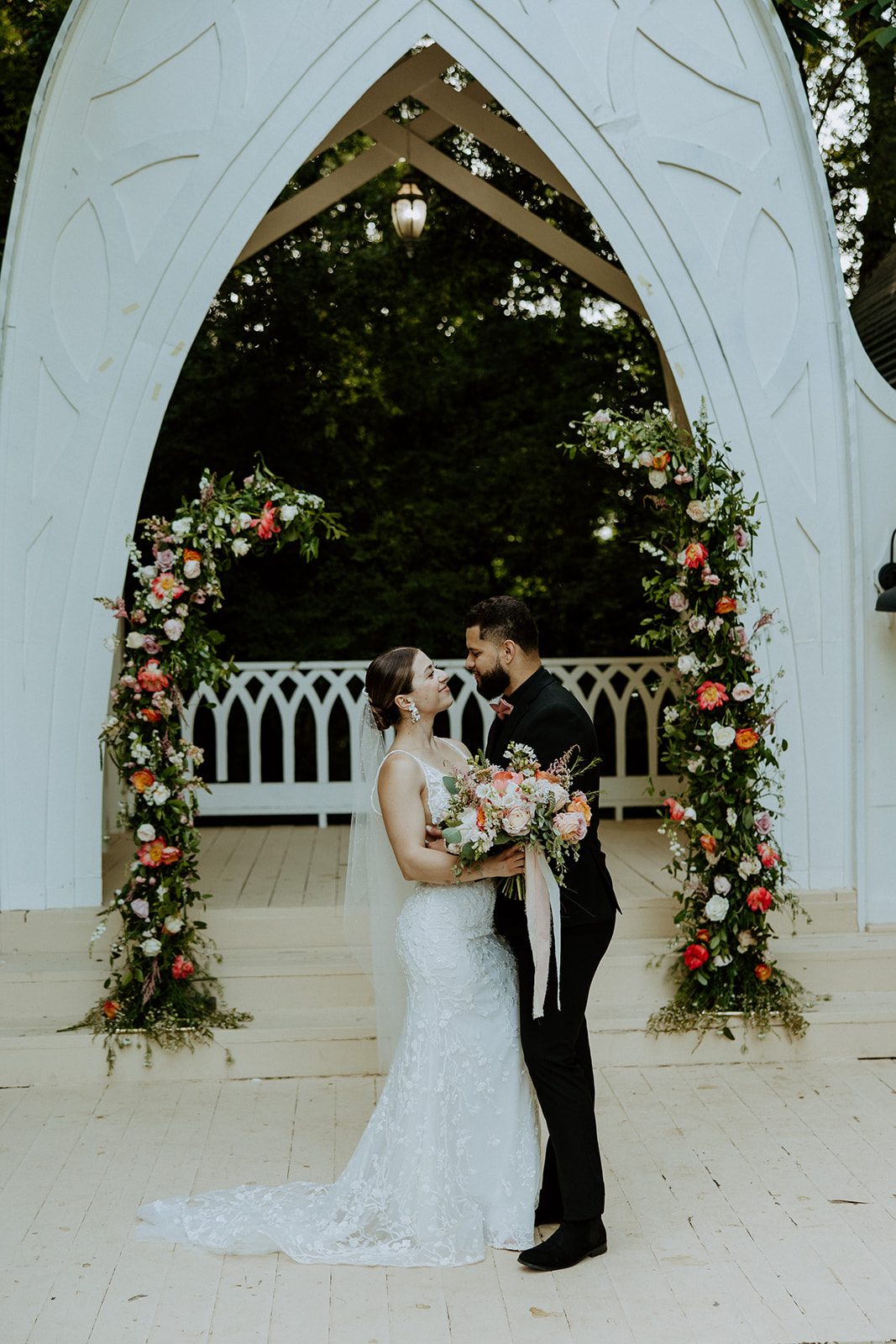 A bride and groom walk down an outdoor aisle holding hands, with empty chairs and an arch structure in the background at wildflower 301