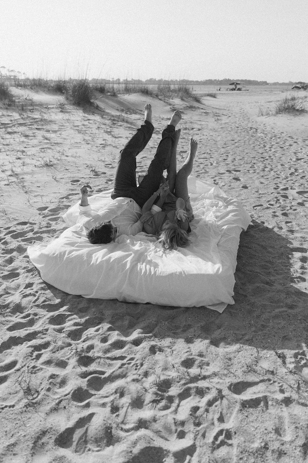 A man and a woman lie on an airmatress on a sandy beach, smiling and holding hands on Tybee Island