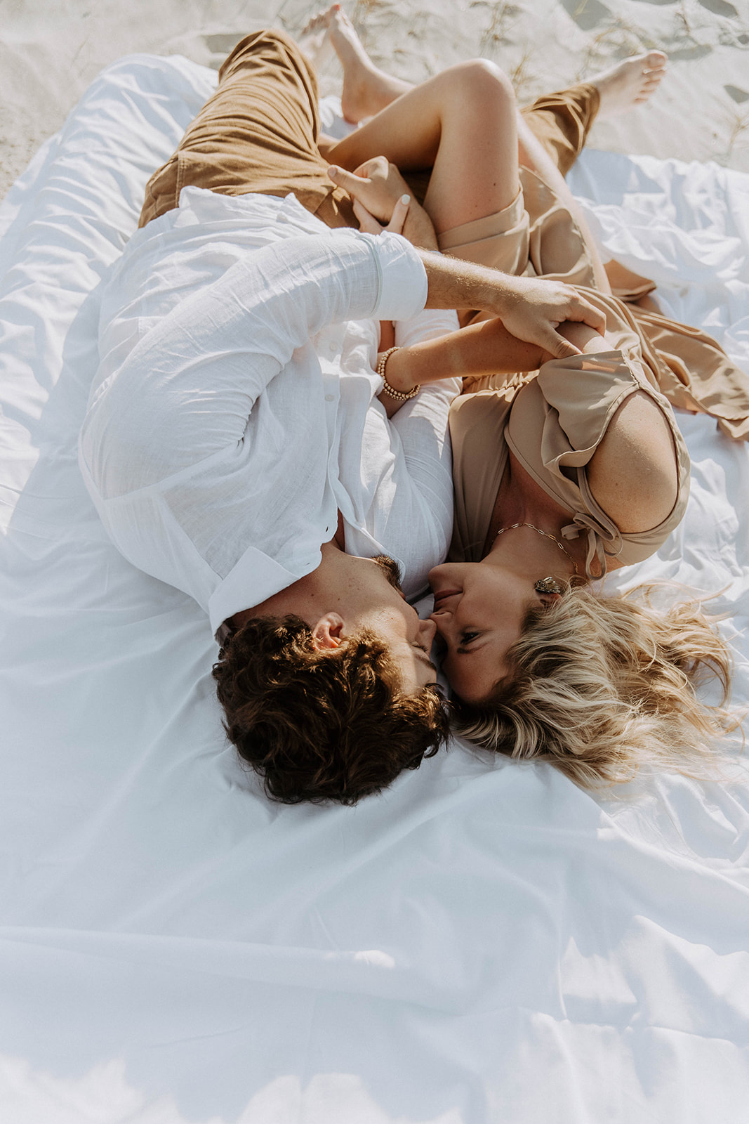 A man and a woman lie on an airmatress on a sandy beach, smiling and holding hands on Tybee Island