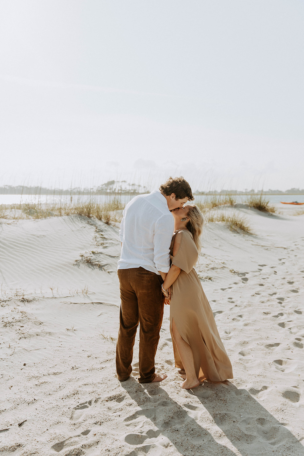 A couple walks hand in hand on a sandy beach under a clear sky on Tybee Island