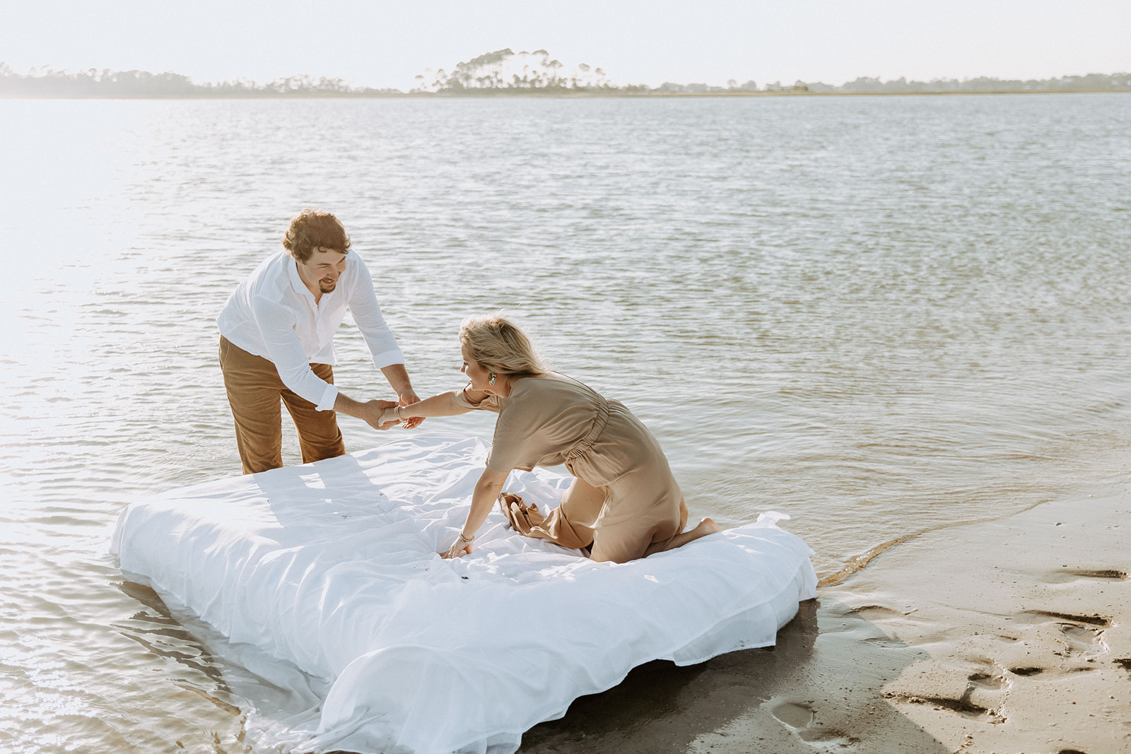 Two people lie on a mattress floating on a calm body of water, appearing relaxed and at ease on Tybee Island