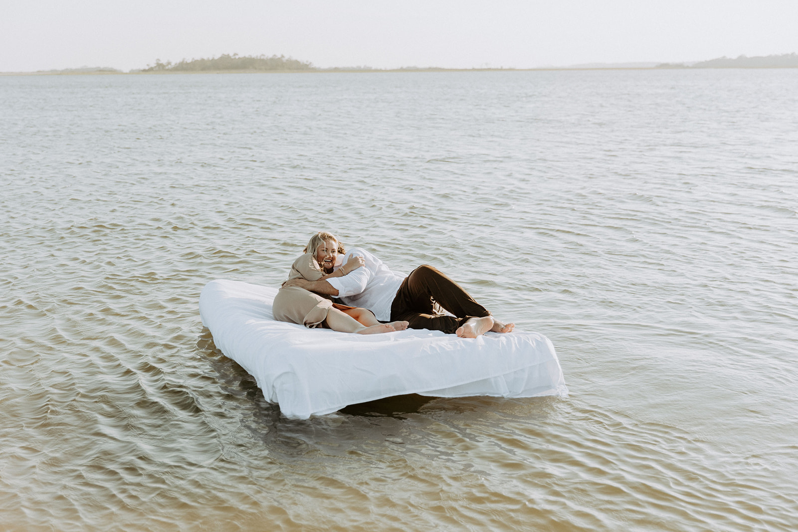 Two people lie on a mattress floating on a calm body of water, appearing relaxed and at ease on Tybee Island