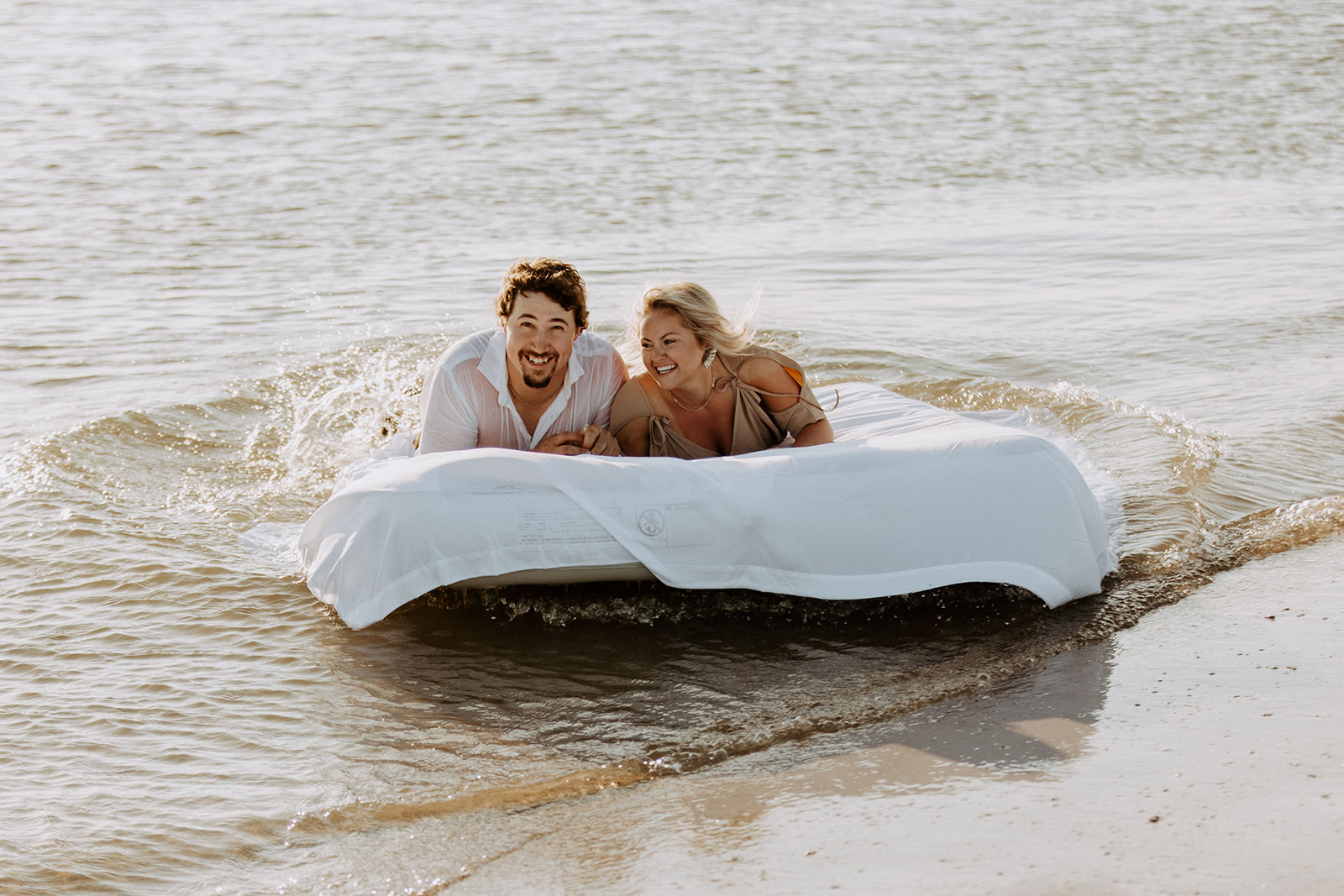 Two people lie on a mattress floating on a calm body of water, appearing relaxed and at ease on Tybee Island