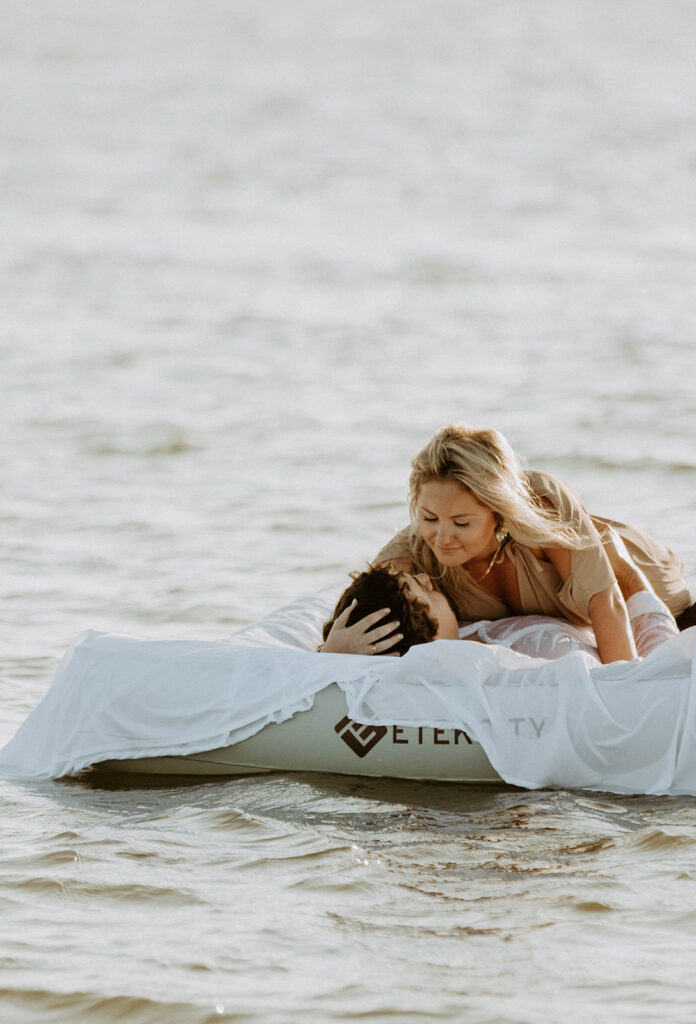 Two people lie on a mattress floating on a calm body of water, appearing relaxed and at ease on Tybee Island