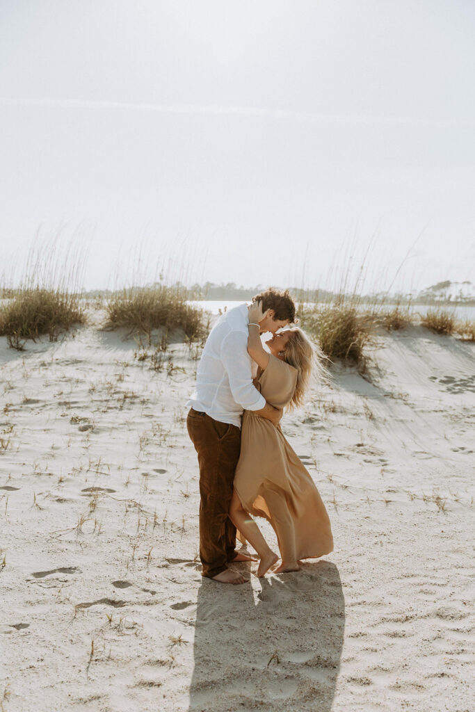 A couple walks hand in hand on a sandy beach under a clear sky on Tybee Island