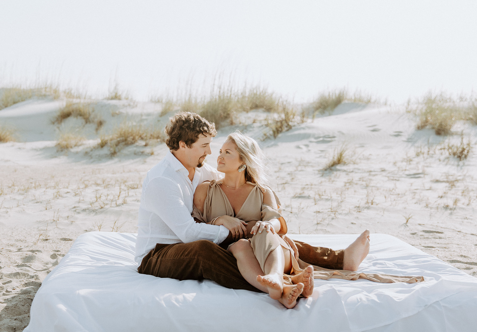 A man and a woman sit closely together on a sandy beach, looking at each other affectionately on Tybee Island