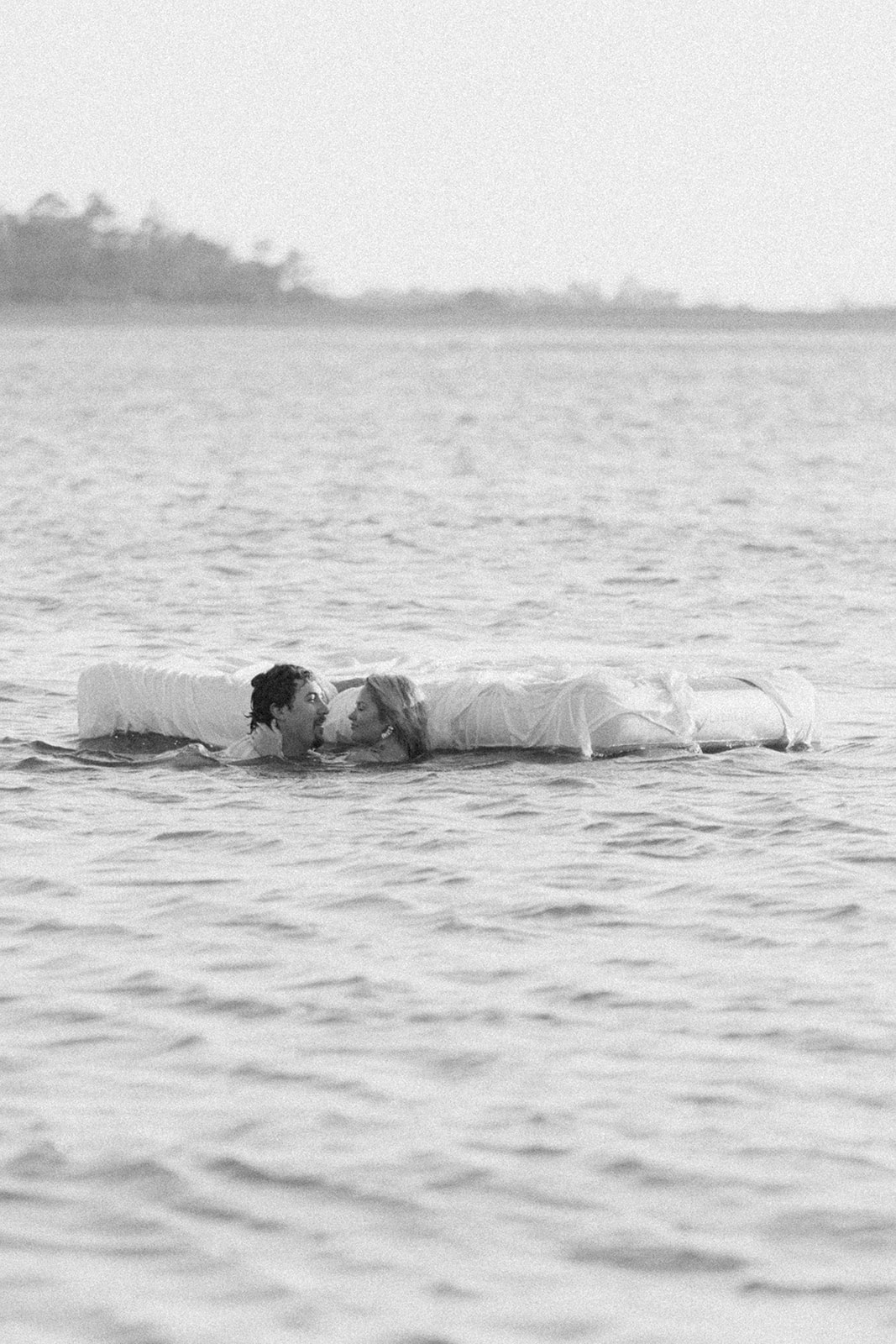 Two people lie on a mattress floating on a calm body of water, appearing relaxed and at ease on Tybee Island