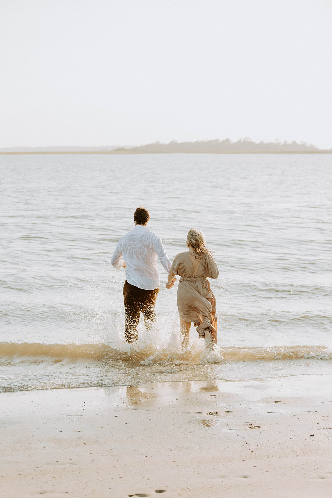 Two people stand in shallow water embracing each other. One wears a white shirt, and the other wears a light-colored dress.