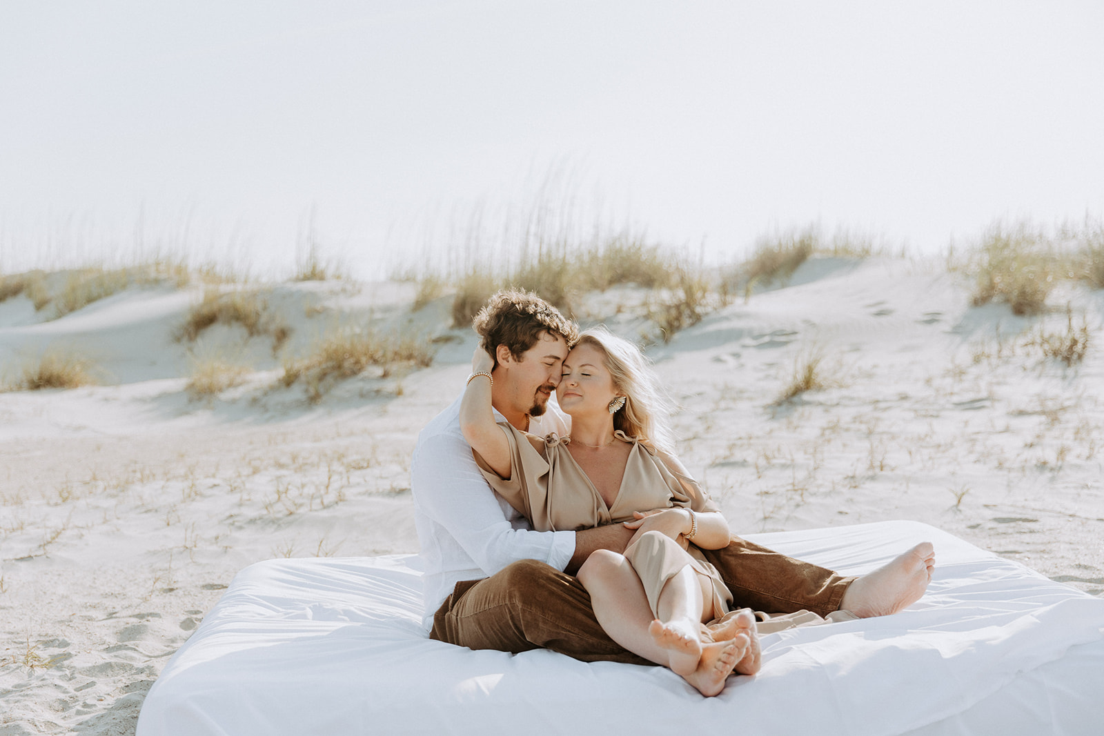 A man and a woman sit closely together on a sandy beach, looking at each other affectionately on Tybee Island