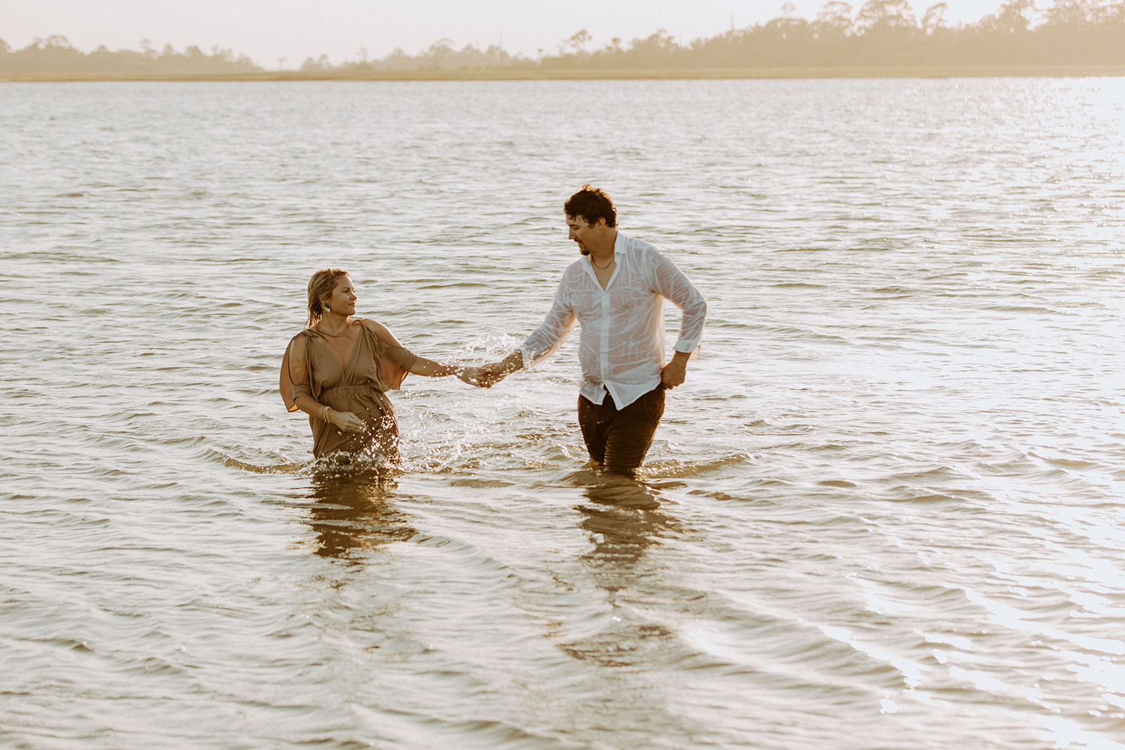 Two people wading through shallow waters while holding hands, with a serene landscape in the background on Tybee Island