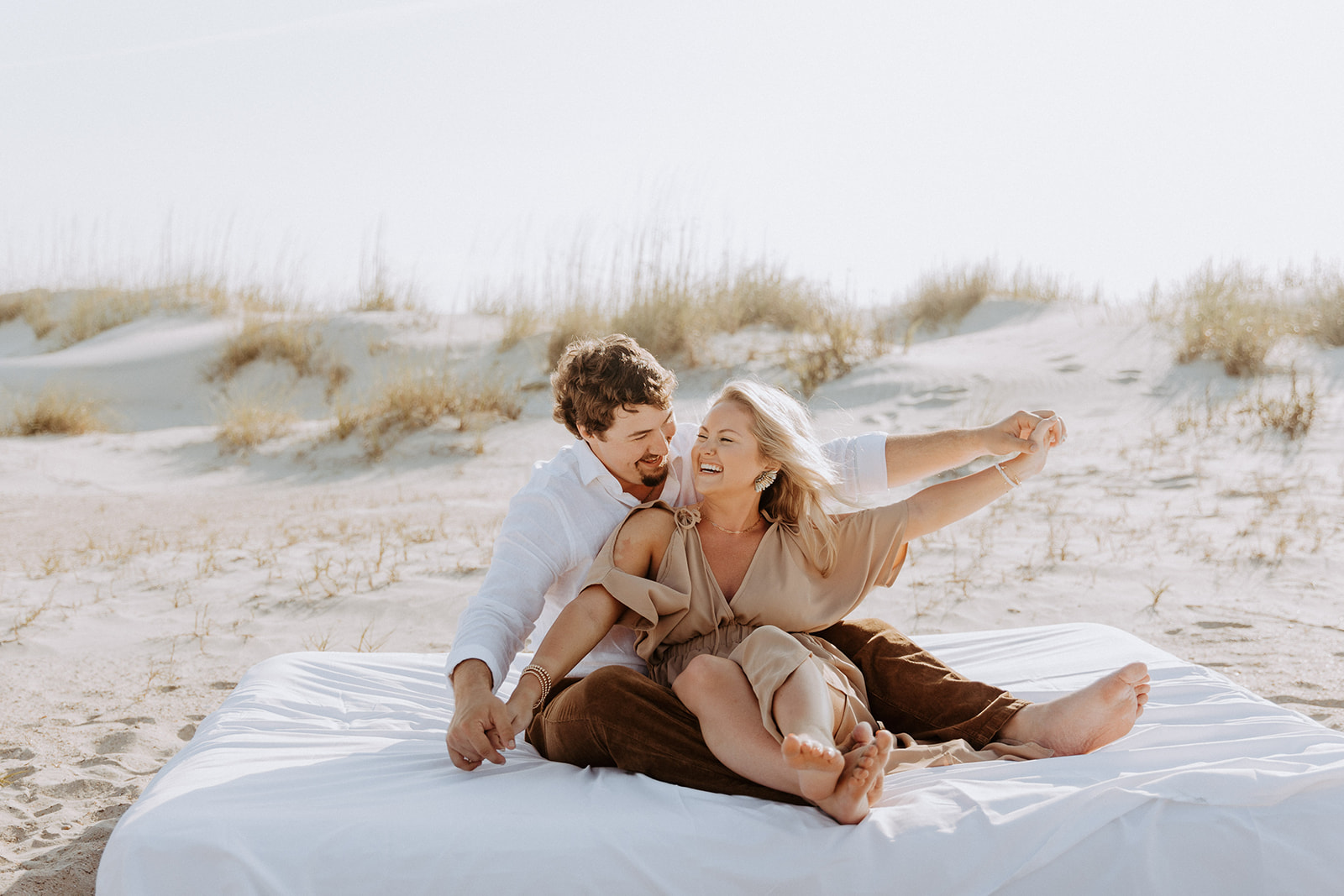 A man and a woman sit closely together on a sandy beach, looking at each other affectionately on Tybee Island