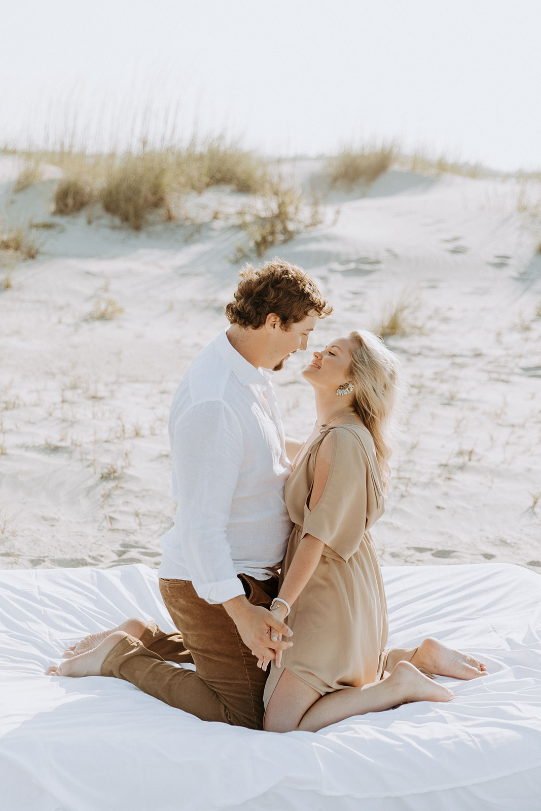 A man and a woman lie on a white blanket on a sandy beach, smiling and holding hands on Tybee Island