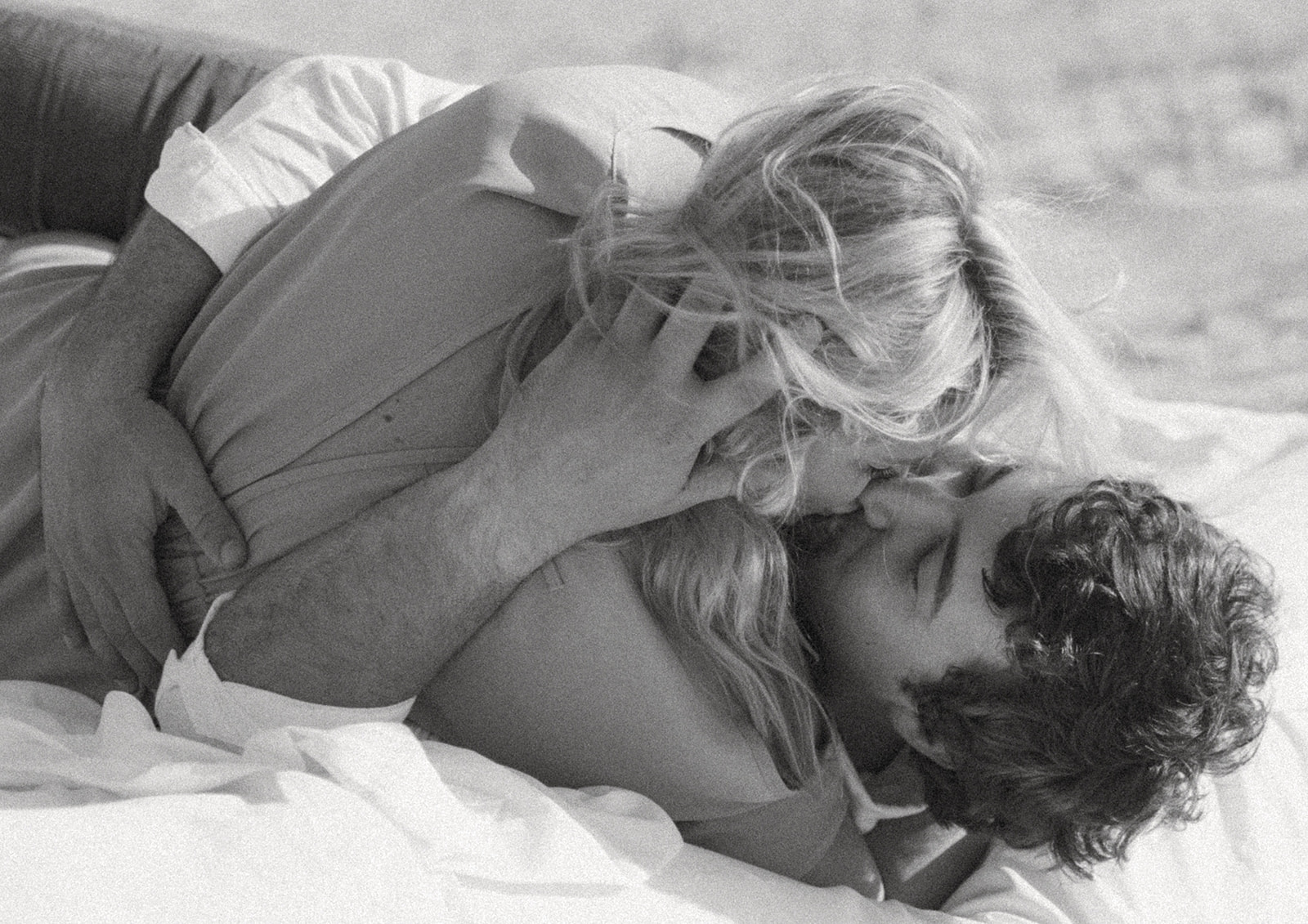 A man and a woman lie on an airmatress on a sandy beach, smiling and holding hands on Tybee Island