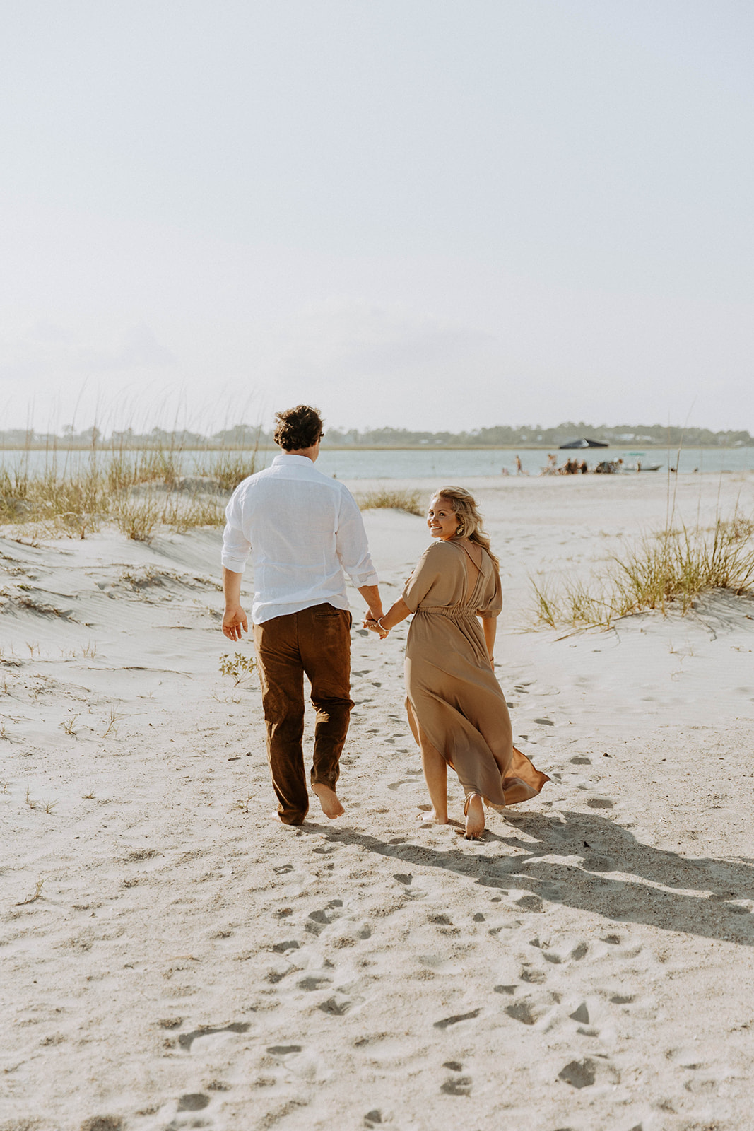 A couple walks hand in hand on a sandy beach under a clear sky on Tybee Island