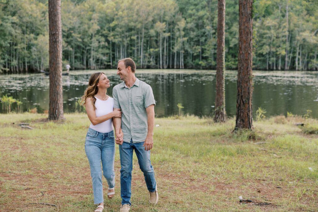 Man and woman holding hands and walking while smiling at each other. 