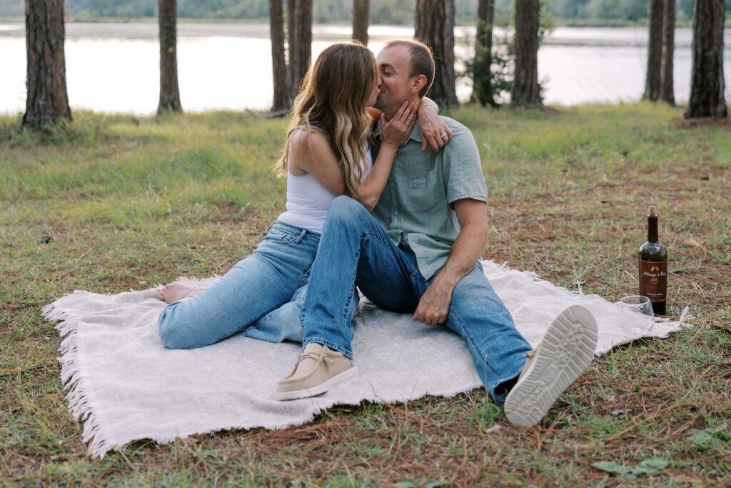 A man and woman sitting on a blanket in the woods kissing