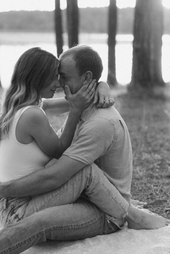 A man and woman embracing with their foreheads touching, trees and water in the background 