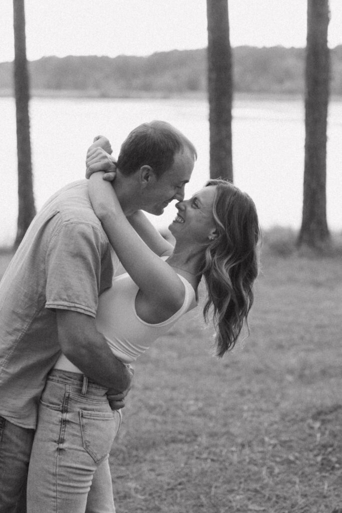 A man and woman embracing in the woods, they are smiling at each other. 